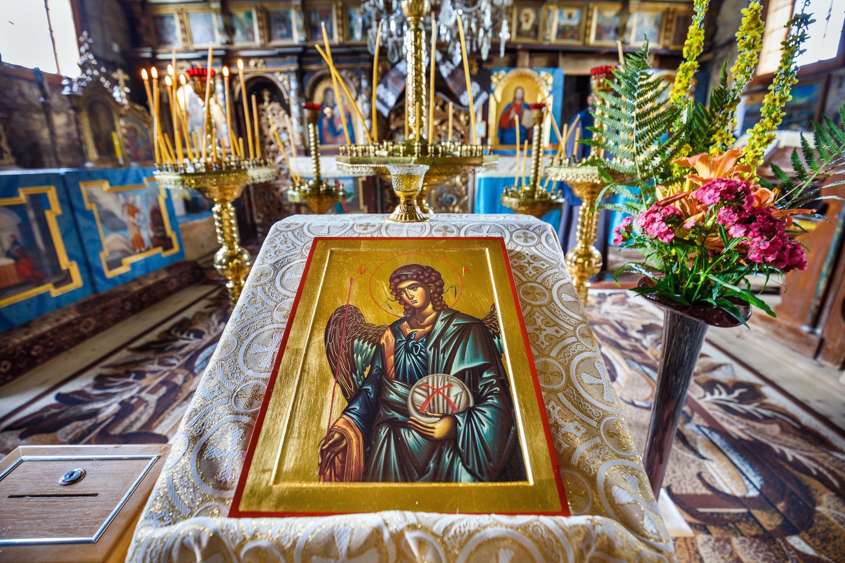 Wizerunek świętego Michała Archanioła, namalowany na desce. Obraz leży na wysokim stoliku z pochyłym blatem, nakrytym biało-złotym płótnem. W tle widoczny ikonostas.